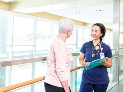 Nurse holding clipboard stands facing a patient