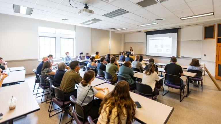 People site at long tables facing a person giving a presentation