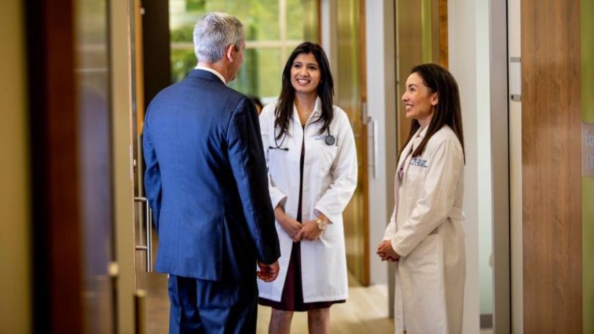 Two people in white lab coats stand facing a person in a blue suit