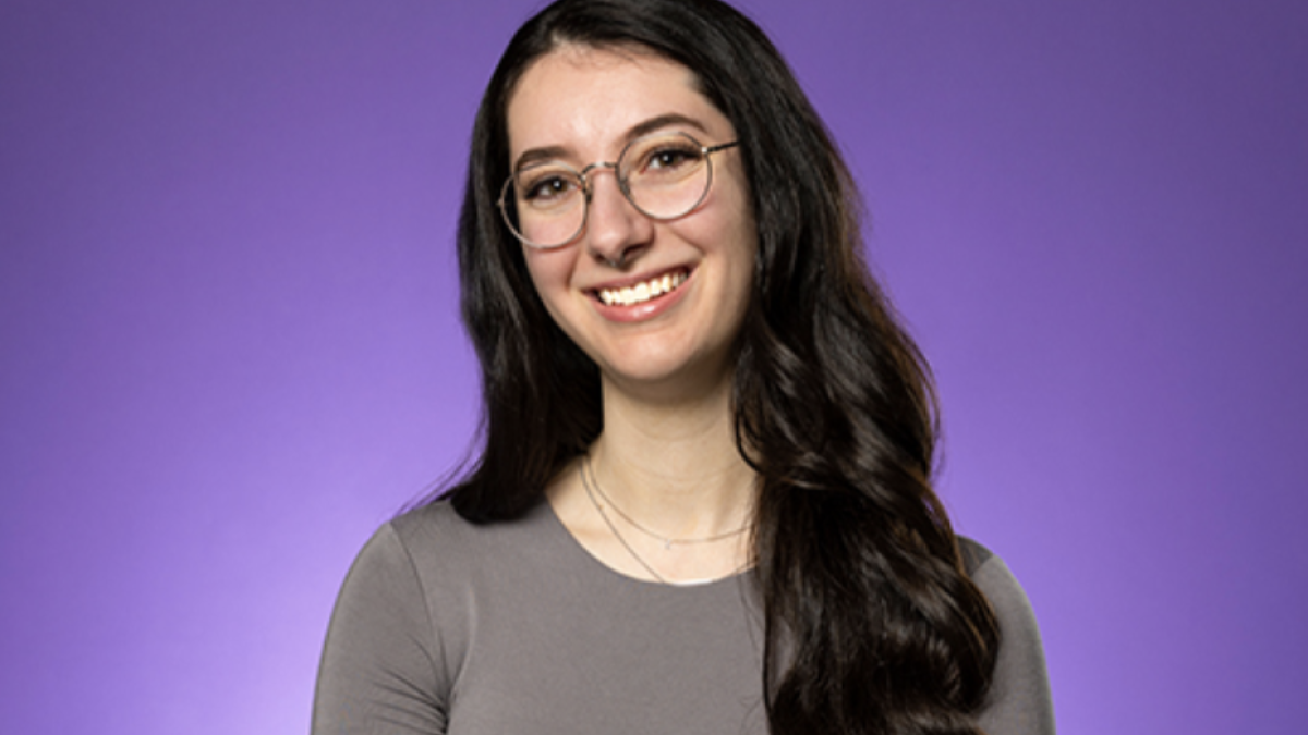 Young woman with long brown hair wearing glasses smiles poses and smiles for photo