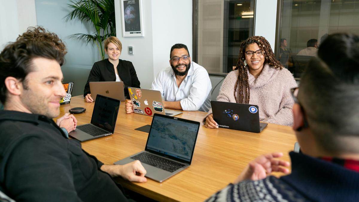 people having a discussion while sitting around a conference table with laptops