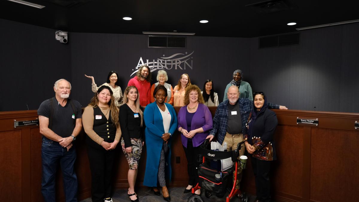 Group of thirteen diverse individuals pose and smile for photo