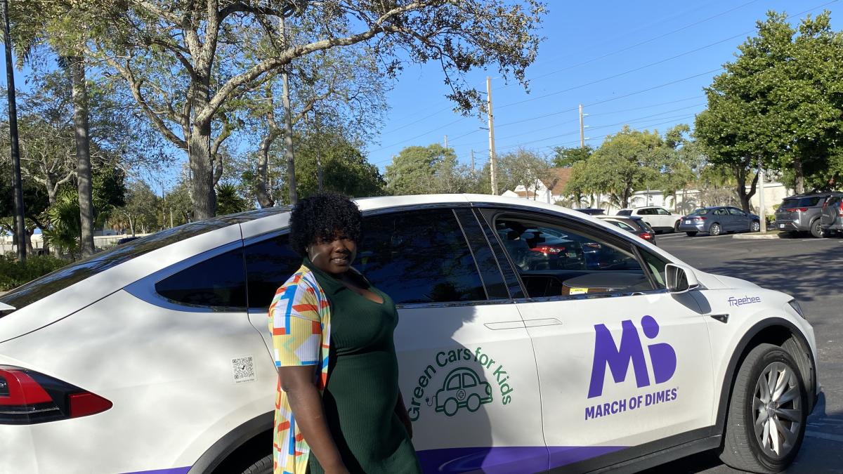 Woman stands next to a parked car and smiles