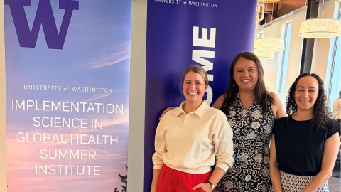 Three women standing and smiling in front of a sign that reads "Implementation Science in Global Health Summer Institute"