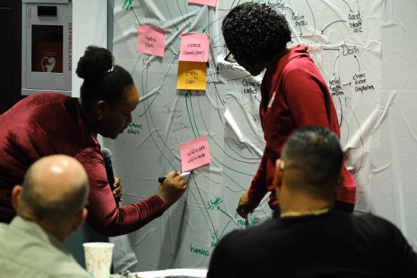 Two people draw on a board while others observe