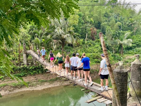 Group of people cross a bridge over water with lots of trees surrounding