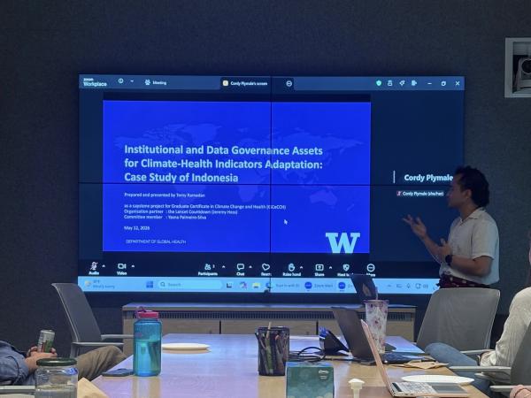 Man standing in front of a screen that says "Institutional and data governance assets for climate-health indicators adaptation: Case study of Indonesia"