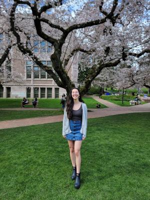 young woman stands under cherry tree on campus