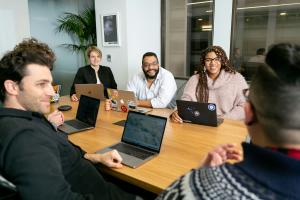 people having a discussion while sitting around a conference table with laptops