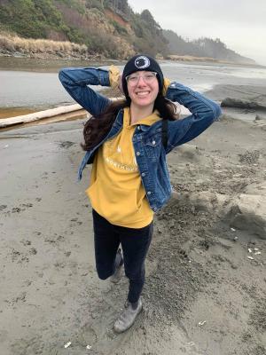 young woman wearing beanie and jacket poses for camera on muddy beach