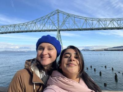 Two women smiling while standing near a bridge and water