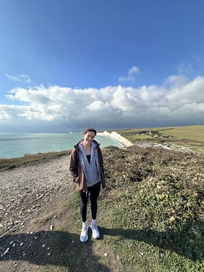 Woman posing and smiling in front of grassy cliffs and body of water